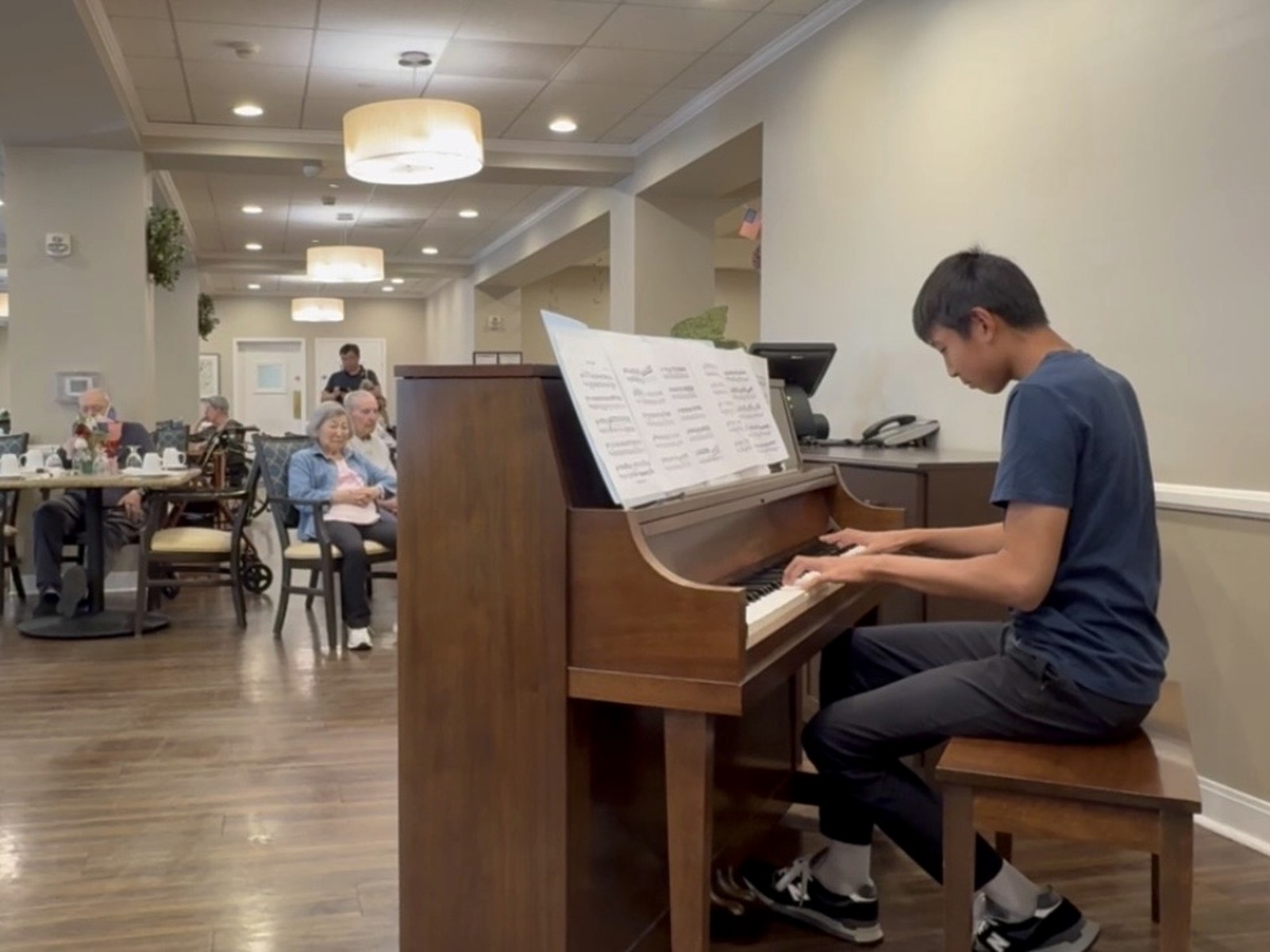A young pianist performing in a senior community dining room.