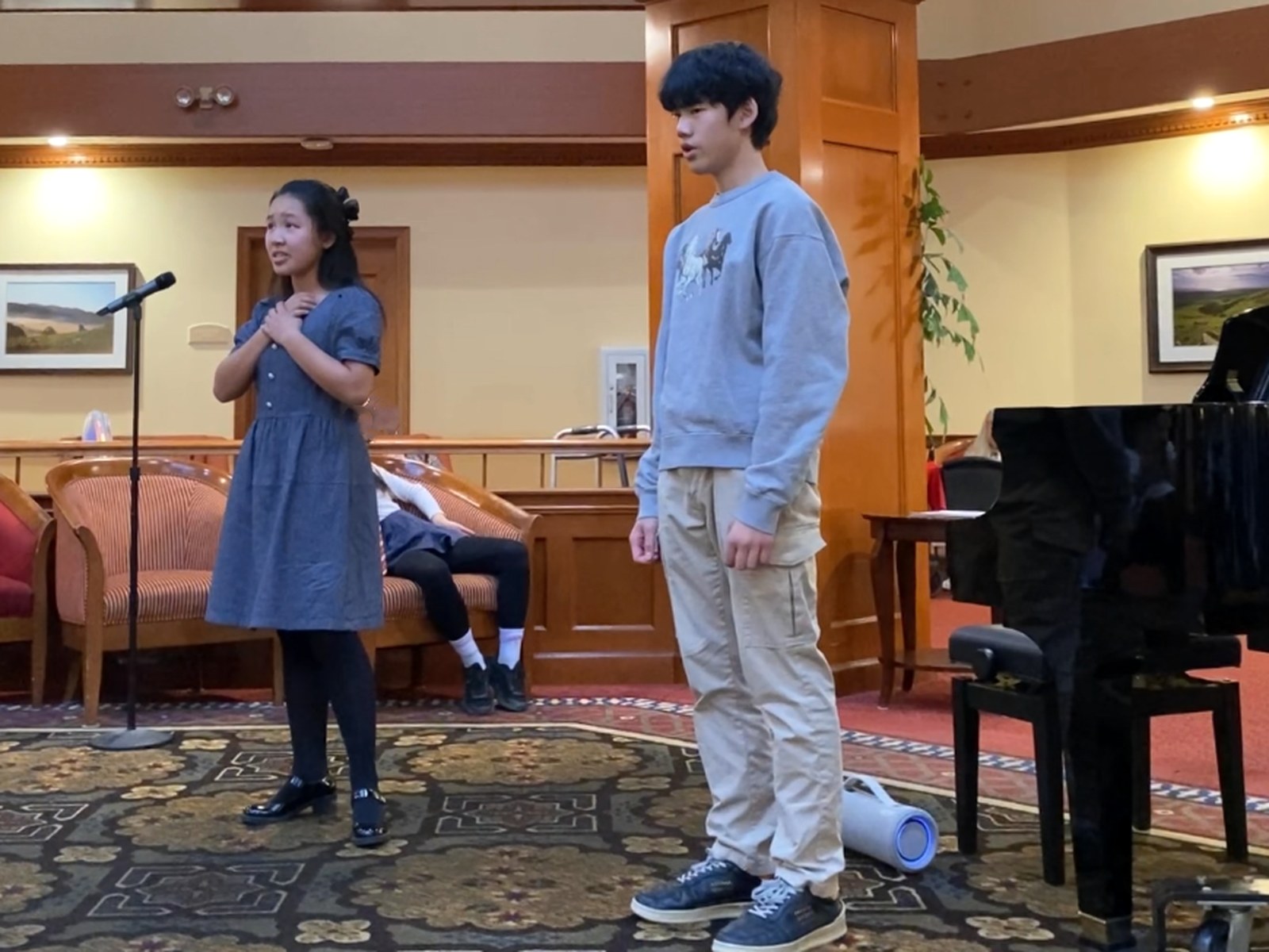 Two student vocalists performing near a piano during an outreach program.
