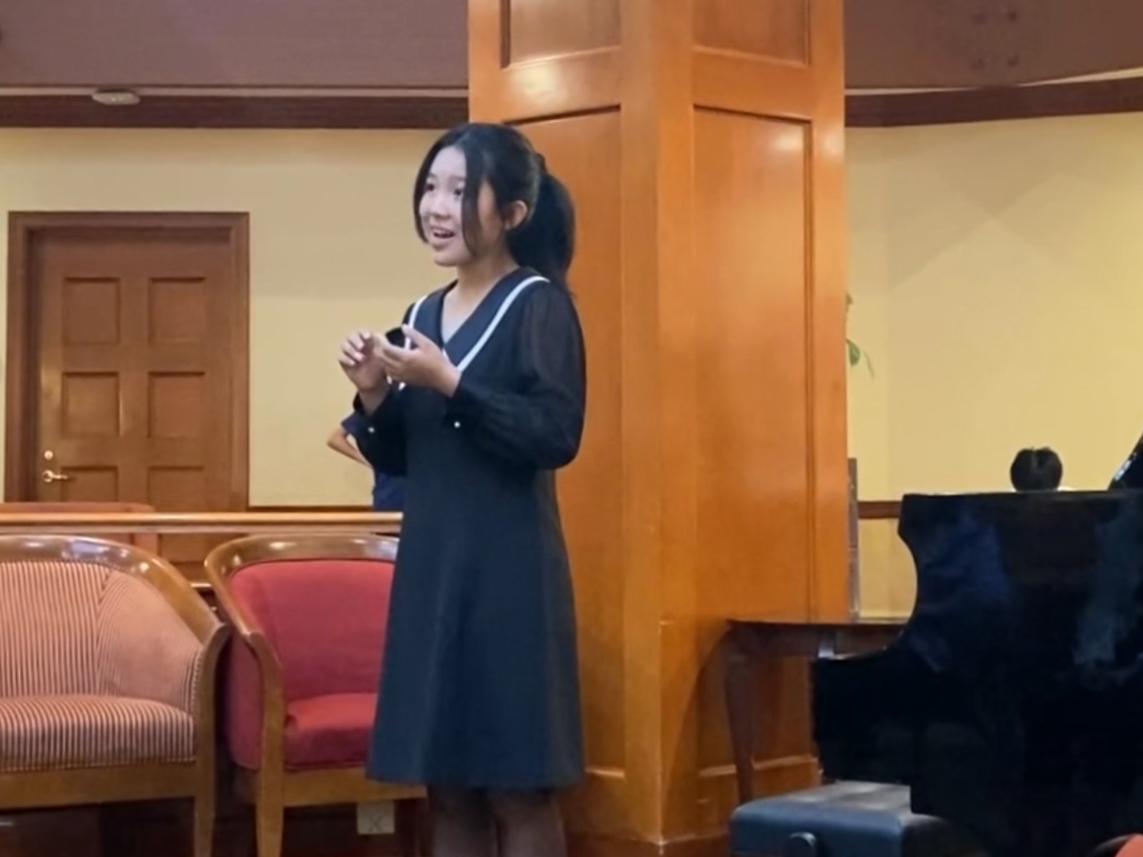 A student vocalist singing beside a piano during an outreach visit.