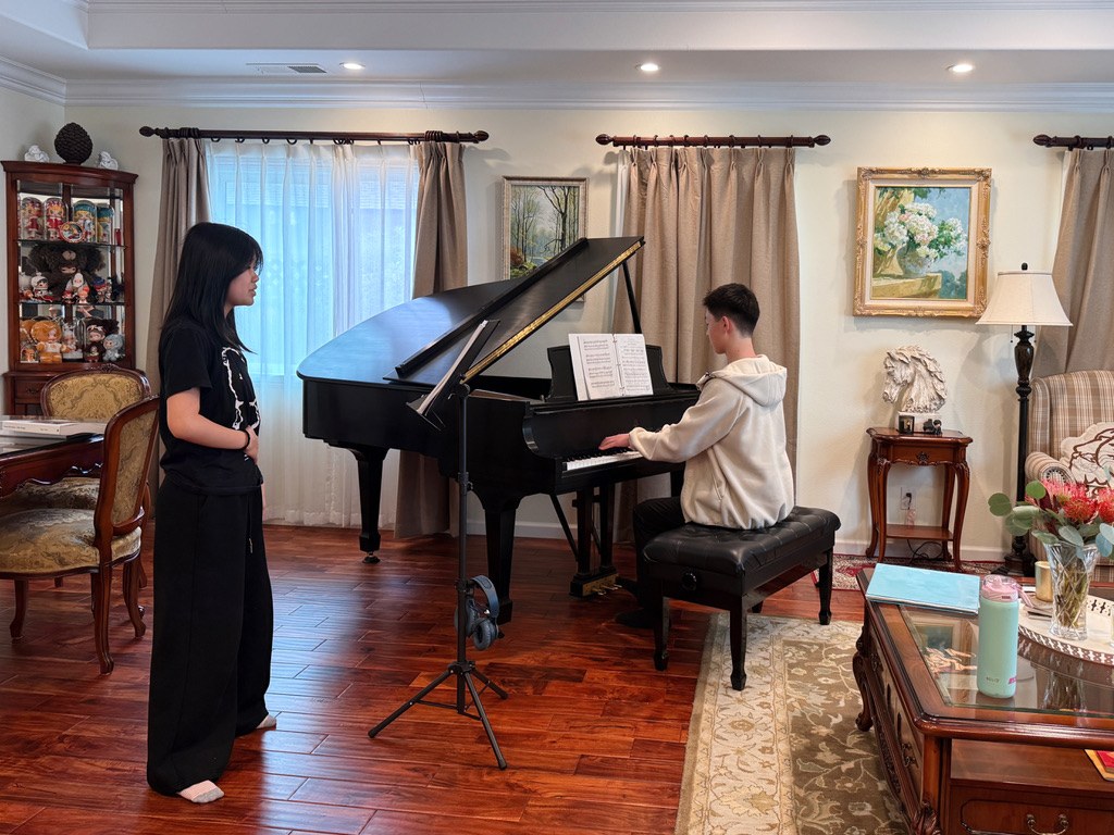 A student vocalist rehearsing beside a grand piano.